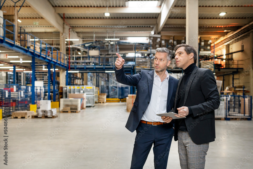Businessman discussing with colleague holding tablet PC in factory Businessman discussing with colleague holding tablet PC in factory