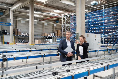 Young businesswoman discussing with colleague by conveyor belt in factory photo