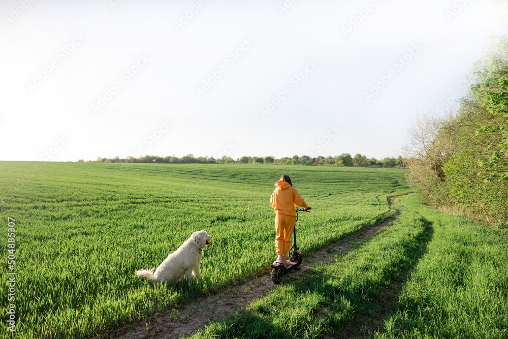 Woman rides electric scooter on green field with a dog Woman rides electric scooter on green field with a dog