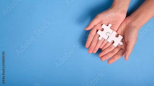 two hands holding and trying to connect couple puzzle piece on blue background. one part of whole. symbol of association and connection. business strategy.