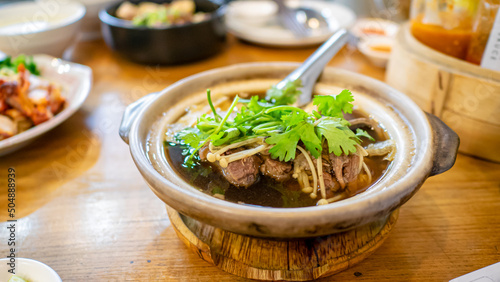 Bak Kut Teh, a close up of Chinese pork rib soup in traditional bowl pot on wooden table at Thai restaurant in Bangkok, Thailand.