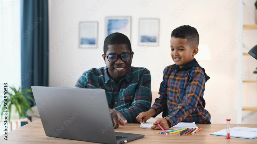 Using laptop. Father with his son is indoors in domestic room together