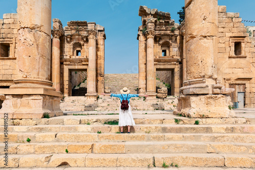 Young tourist standing with hat and open arms  in old city of Jerash, ancient building in Jordan photo