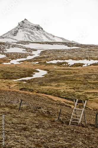 simple wooden landscape across a fence in a partly snow-covered mountainous landscape with moss and rocks near Olvafsvik, Iceland photo