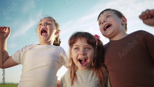 group of kids team hugging a jumping and rejoicing outdoors. happy family teamwork kid dream concept. family children sisters brothers have fun sun hugging in the park in nature