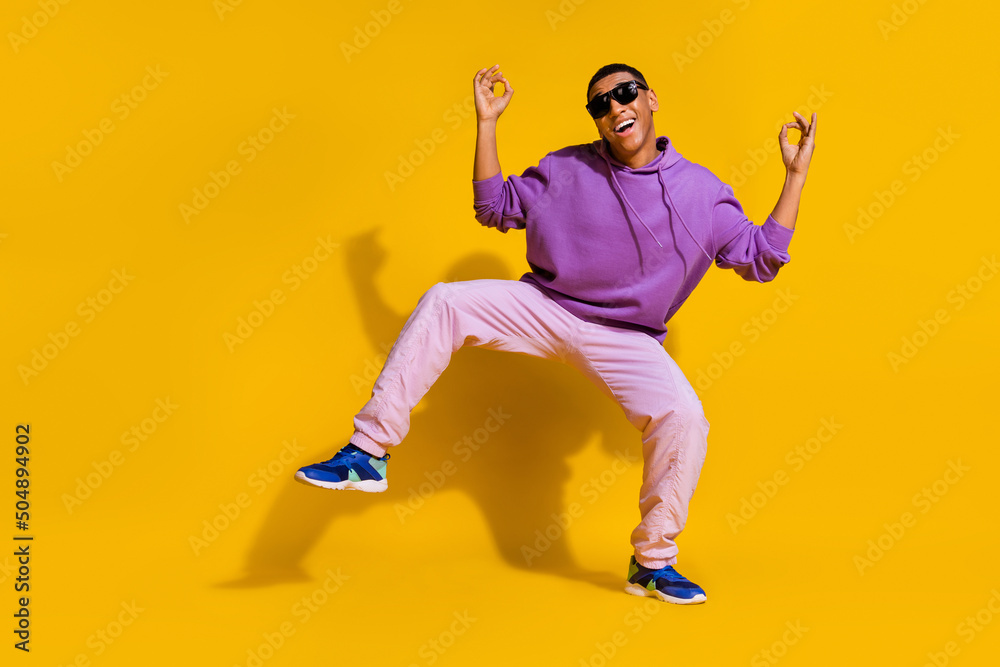 Full length body size view of attractive trendy carefree guy dancing showing ok sign isolated over bright yellow color background Full length body size view of attractive trendy carefree guy dancing showing ok sign isolated over bright yellow color background