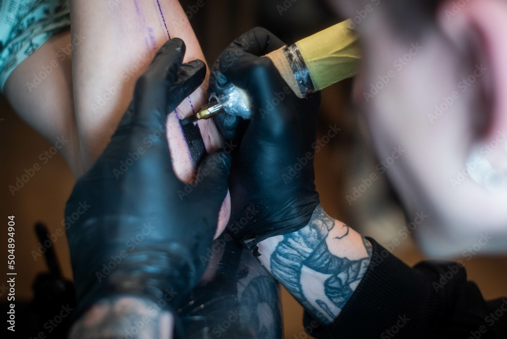 cropped shot of tattooing process on hand in salon. A professional tattoo artist introduces ink into the skin using a needle from a tattoo machine.Professional tattooist working in studio. cropped shot of tattooing process on hand in salon. A professional tattoo artist introduces ink into the skin using a needle from a tattoo machine.Professional tattooist working in studio.