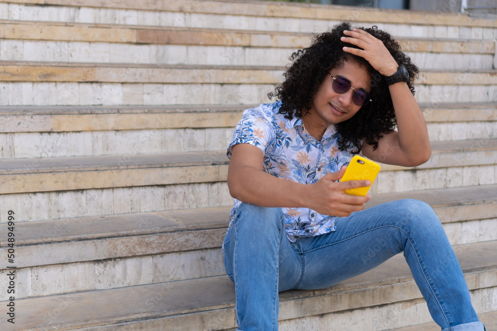 Portrait of a man with long curly hair, using a cell phone.