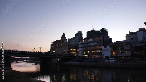 KYOTO, JAPAN - DEC 2021 : View of Kamogawa (River) and cityscape of Kawaramachi downtown area in sunset. Time lapse shot, dusk to night. Riverbanks are popular walking spots for residents and tourists