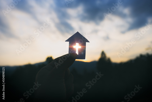 Hand holding home cross shapes. with light of sunset background, christian silhouette concept.
