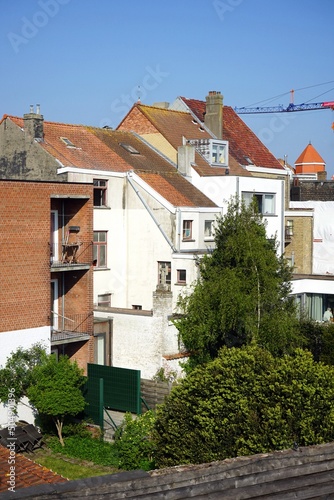 Weiße Wohnhäuser mit Spitzgiebel und rotbraunen Ziegeldächern mit großem Baukran vor blauem Himmel im Sonnenschein in Knokke-Heist an der Nordsee bei Brügge in Westflandern in Belgien photo