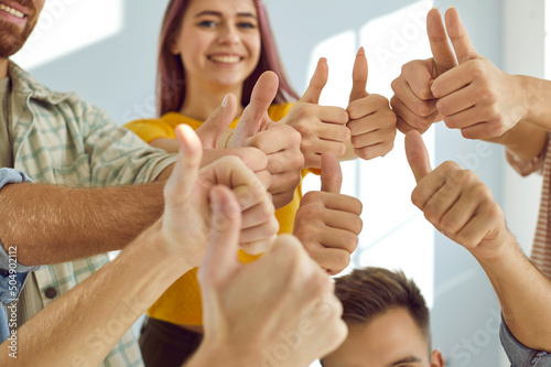 Group of happy, smiling, young people giving thumbs up all together. Team of cheerful, satisfied male and female university students showing that they agree with a good suggestion. Hands close up shot