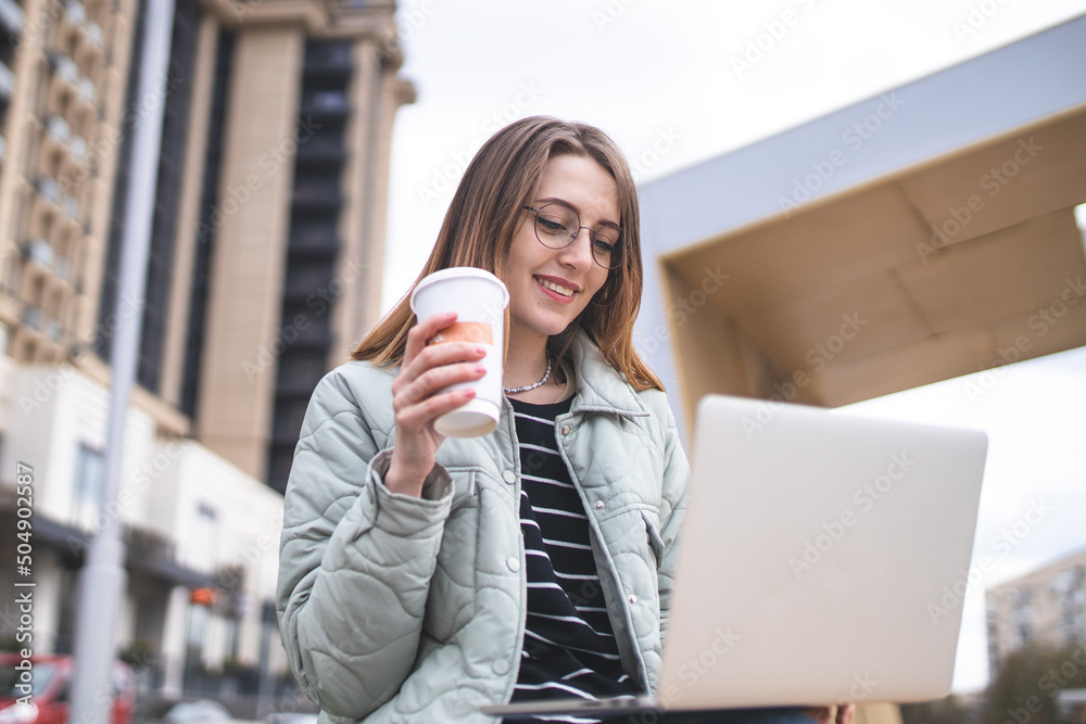 Fototapeta premium Girl drinking coffee on the summer playground of a cafe. Street photography. Carefree girl enjoys the good weather. 