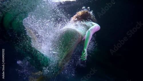 a mermaid swims away into the dark abyss in streams of bubbles. view from the back. the middle plan photo