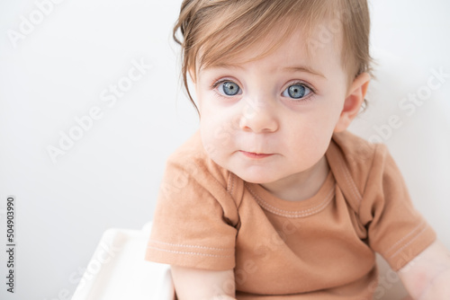 portrait of cute baby girl 10 months with blue eyes in brown bodysuit on white background