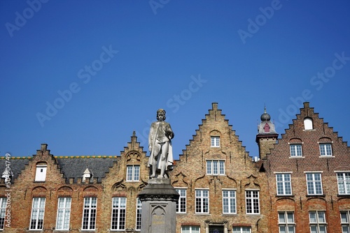 Statue von Hans Memling am Woensdagmarkt mit schönen alten Treppengiebeln aus Backstein vor blauem Himmel im Sonnenschein in den Gassen der Altstadt von Brügge in Westflandern in Belgien photo