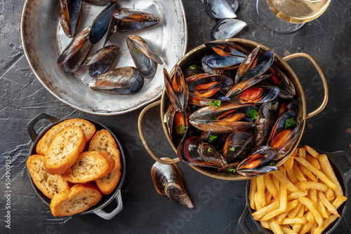 Cooked mussels with French fries and toasted bread, with wine, shot from the top on a black stone background