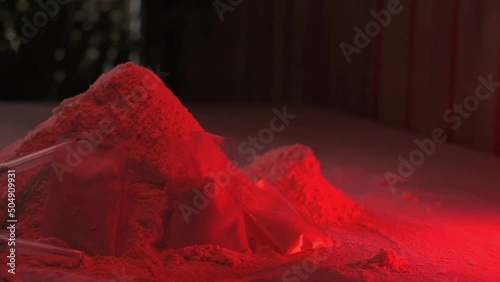 Drugs, drug dealer's house. Cocaine packaged in sachets, scales: tablets and syringes in neon light. Illegal, entry. Syringes and hard drugs.