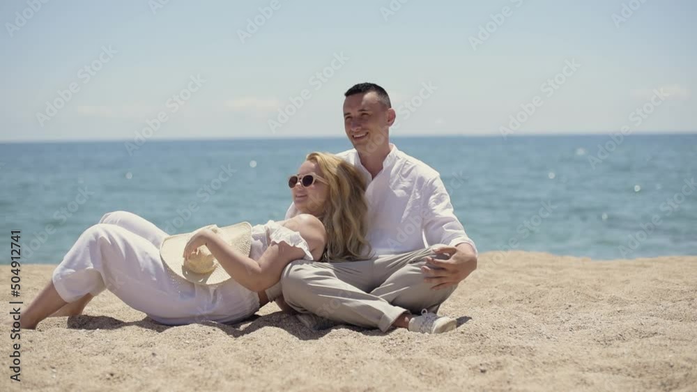 The couple is relaxing on the beach. A girl with a guy lies on the background of the ocean in white clothes, relaxes, summer vacation. The couple is relaxing on the beach. A girl with a guy lies on the background of the ocean in white clothes, relaxes, summer vacation.