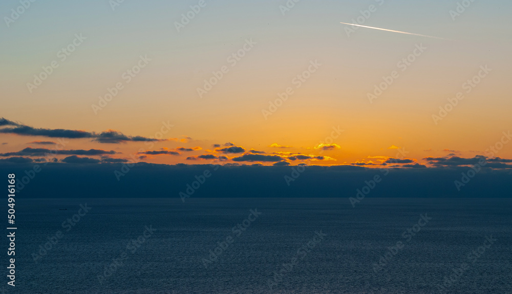 Bright sunset over the sea. Skyline with clouds. Airplane trail in the sky.