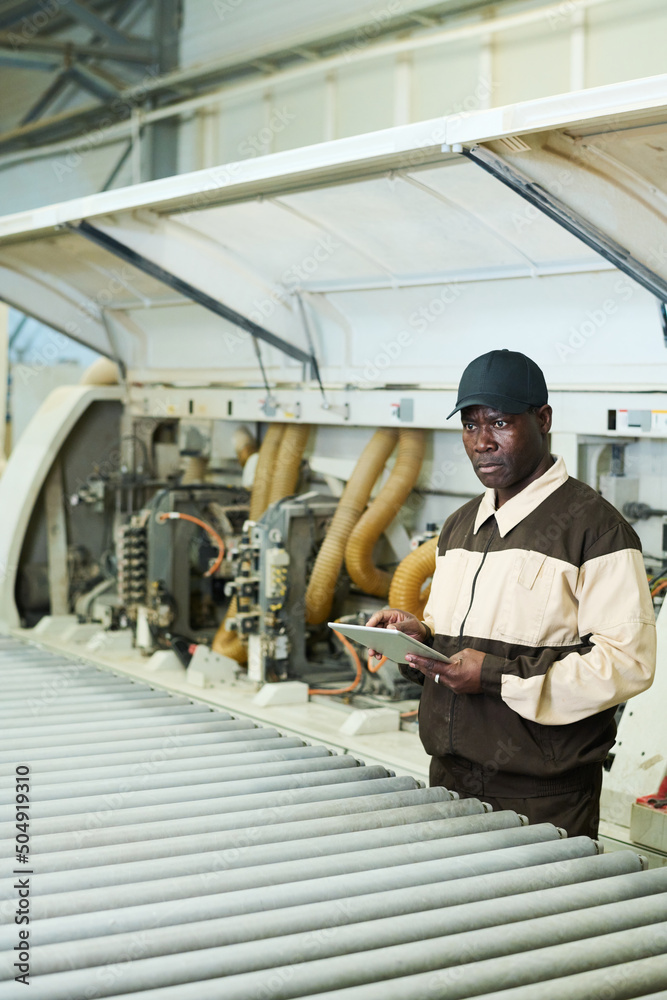 African serious worker in uniform using digital tablet during his work with machine at factory