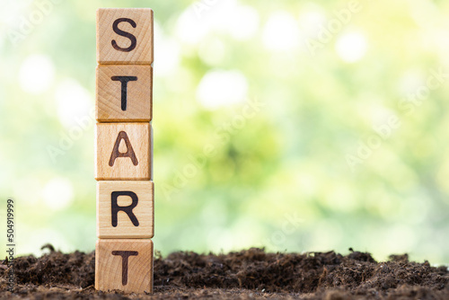 Wooden blocks lie on a wooden table against the backdrop of a summer garden and create the word START.