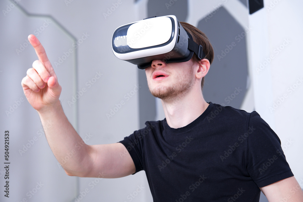 Happy young man, guy using, wearing a modern device virtual reality headset mask or 3D, AR, VR glasses, playing the game, pointing with hand, finger to camera. People and technology metaverse concept. Happy young man, guy using, wearing a modern device virtual reality headset mask or 3D, AR, VR glasses, playing the game, pointing with hand, finger to camera. People and technology metaverse concept.