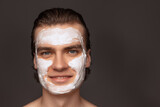 Moisturizing face mask. One man with perfect well-kept skin using face cream mask isolated over grey background. Cosmetics, health care, skin care, beauty