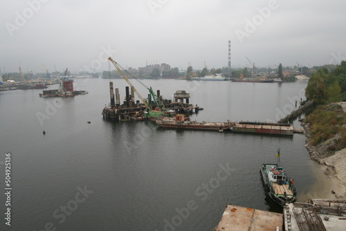 Cranes on barges build towers for a bridge in the middle of the Dnieper River in downtown Kyiv