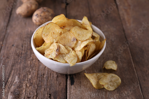 Bowl with potato chips and potatoes on wooden background