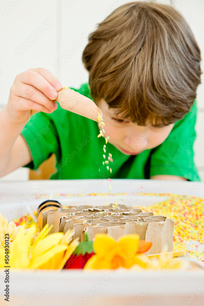 Boy is playing with artificial flowers, bees and a paper