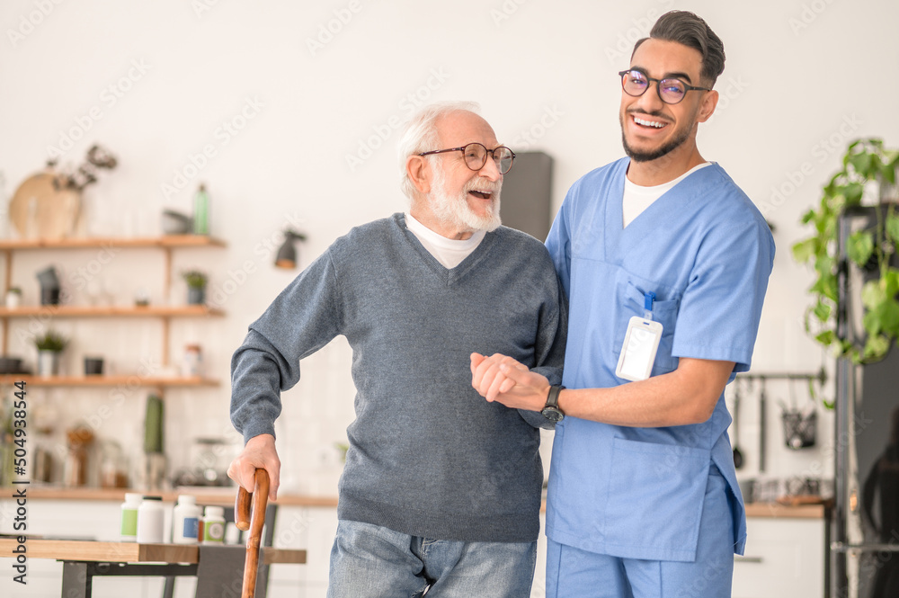 Nurse helping his senior patient to walk with a cane - obrazy, fototapety, plakaty 