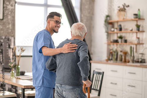 Nurse helping his patient to walk with a walking stick