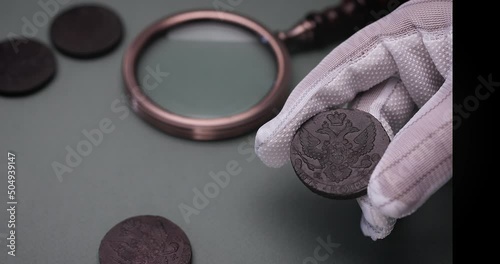 Numismatics. Old collectible coins on the table.  A collector in special gloves holds an old coin. photo