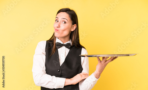 young adult pretty woman shrugging, feeling confused and uncertain. waiter and tray concept photo