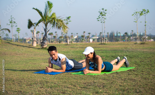 Happy young sporty couple exercising together in green park. Man and woman relaxing on yoga mat. Healthy lifestyle concept