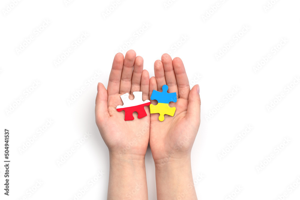 Children's hands hold two puzzles with flags of Poland and Ukraine on white background. Unity solidarity help concept	