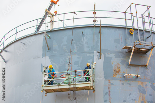 The male worker holding an industrial painting brush used for shell plate tank oil surface painted gray color