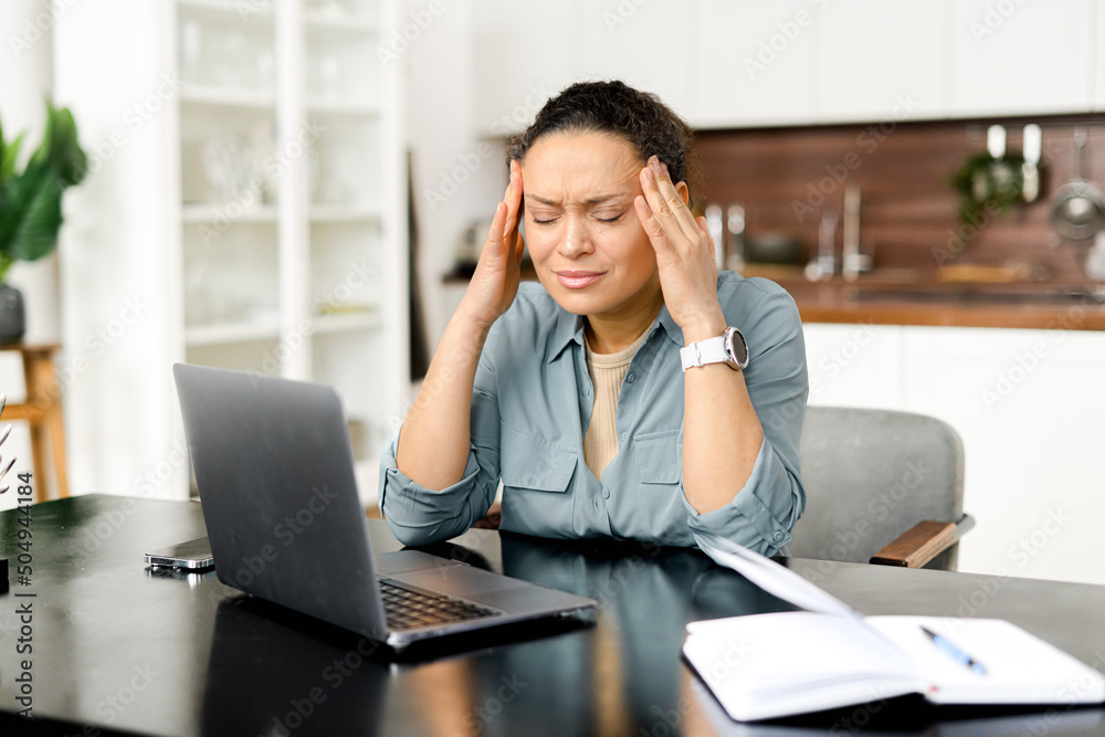 Frustrated young woman using laptop computer suffering from headache, sitting in home office and holding head with hands, feels sick and unwell, burnout and overworked Frustrated young woman using laptop computer suffering from headache, sitting in home office and holding head with hands, feels sick and unwell, burnout and overworked