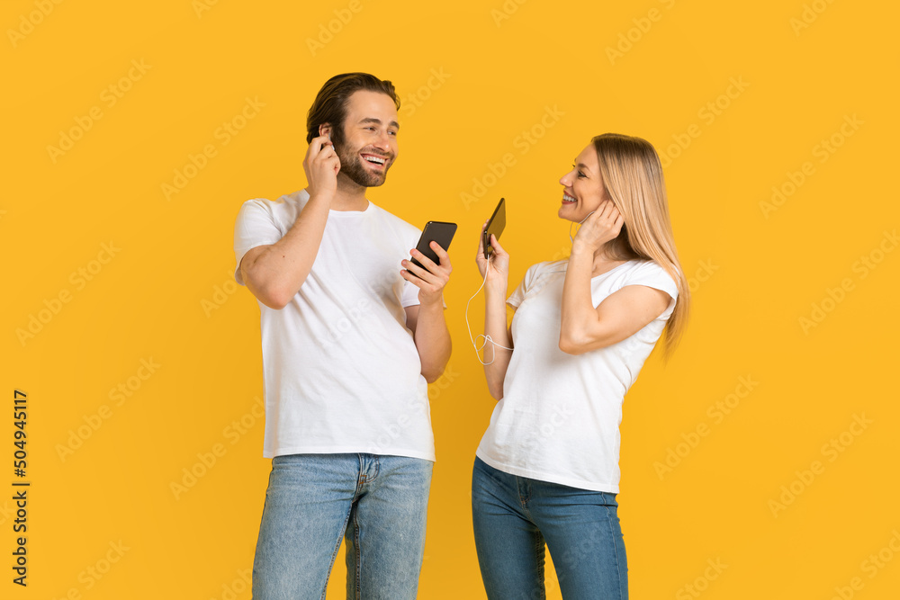 Happy millennial european male and female in white t-shirts with smartphones, puts headphones and listen music Happy millennial european male and female in white t-shirts with smartphones, puts headphones and listen music