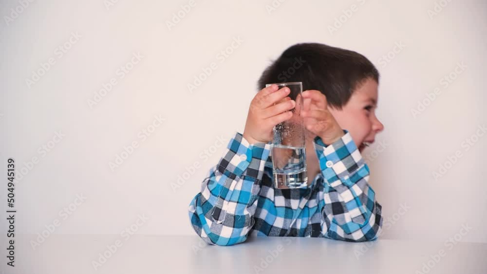 A handsome boy of 4 years drinks water, smiles and looks away, talks, takes a glass in his hands A handsome boy of 4 years drinks water, smiles and looks away, talks, takes a glass in his hands