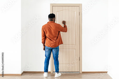 Fotografie, Obraz Black Male Knocking At Door Standing Back To Camera Indoors