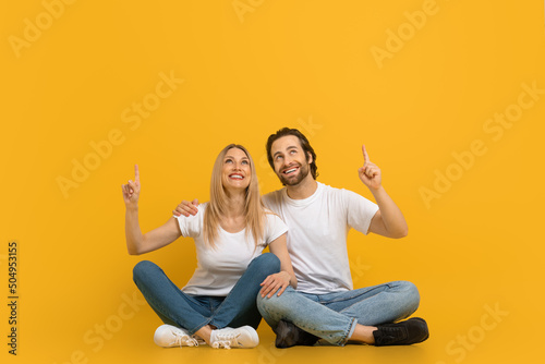 Cheerful millennial european male with beard and female hugging, sit on floor, show fingers up at free space photo