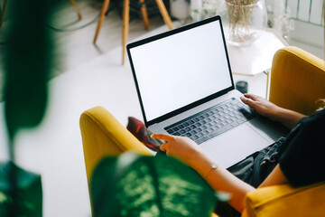 Young caucasian woman sitting on sofa at home and using laptop computer with white blank screen, mock-up.
