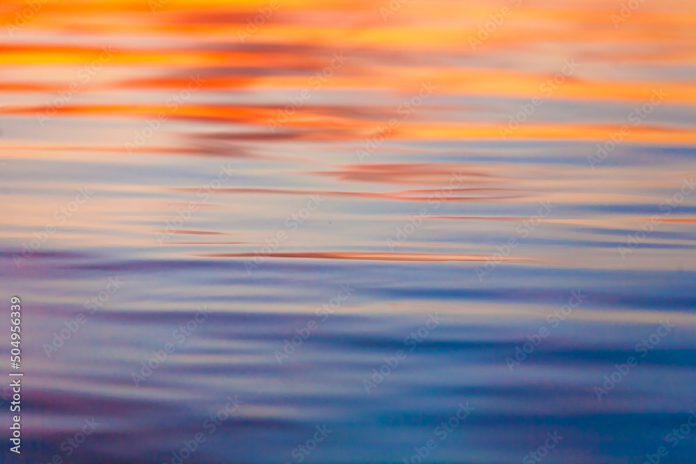 Defocused abstract background of bright orange and blue waves on river during sunset 