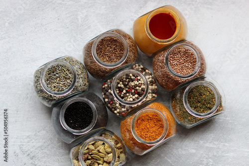 Close up photo of various spices in glass jars. Cardamom, flax seeds, mixed pepper, lavender, curry and turmeric. 