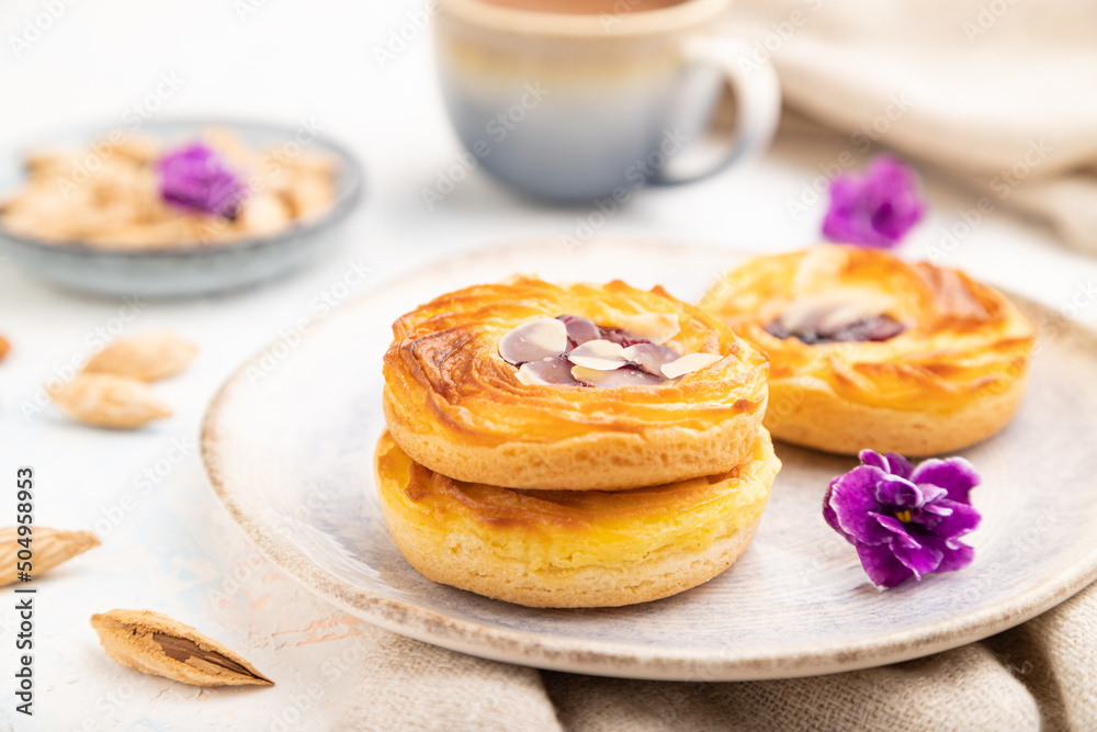 Small cheesecakes with jam and almonds with cup of coffee on a white concrete background. Side view, selective focus. Small cheesecakes with jam and almonds with cup of coffee on a white concrete background. Side view, selective focus.