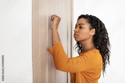 Foto Serious Black Lady Knocking At The Door Of Apartment Indoor