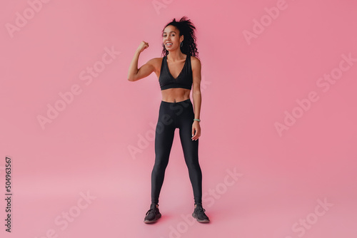 attractive black african american woman in black leggins fitness outfit on pink background © mary_markevich