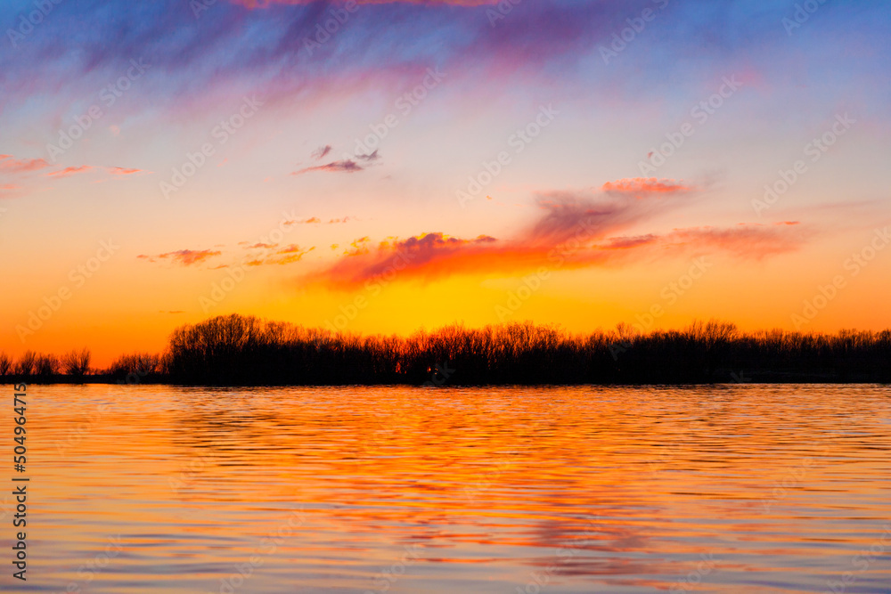 Orange, yellow and purple sunset on river with dark colorful clouds in sky with trees reflection in water Orange, yellow and purple sunset on river with dark colorful clouds in sky with trees reflection in water